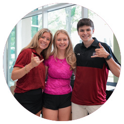 three students with their arms around each other sport the spurs up hand sign while smiling