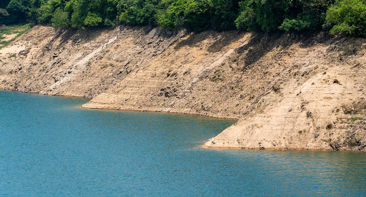 An earthen dam surrounded by blue water and green trees.
