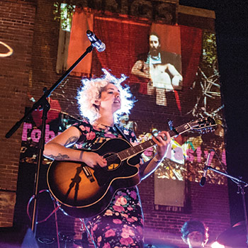 Musicians on stage playing a guitar with bright lights shining on them. 