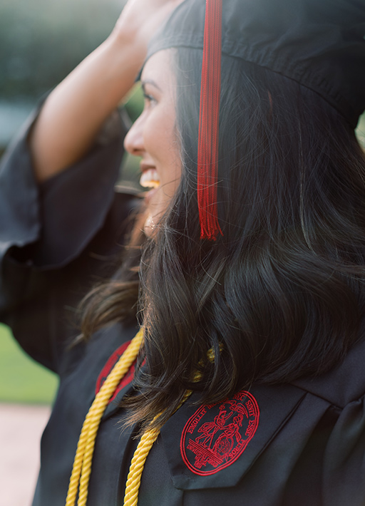 Student wearing graduation cap and gown adjusting her hat smiling in the sun..