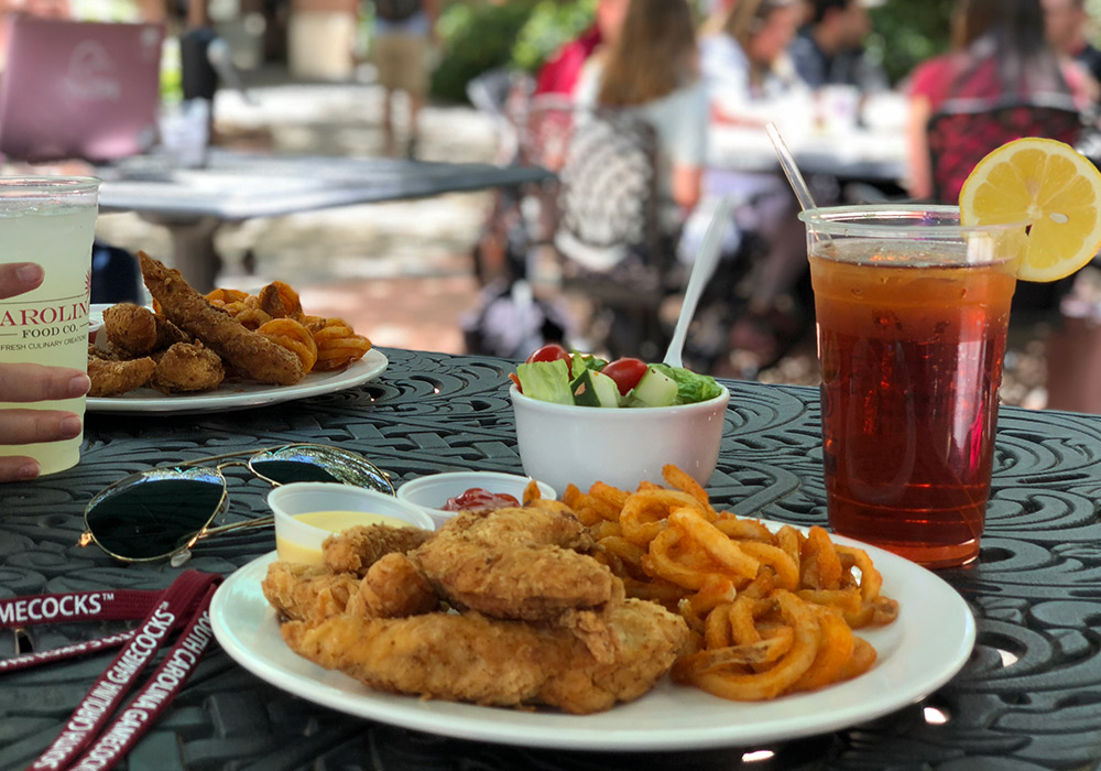 A plate of chicken fingers and curly fries on an outdoor patio table with a cup of sweet tea with a lemon.