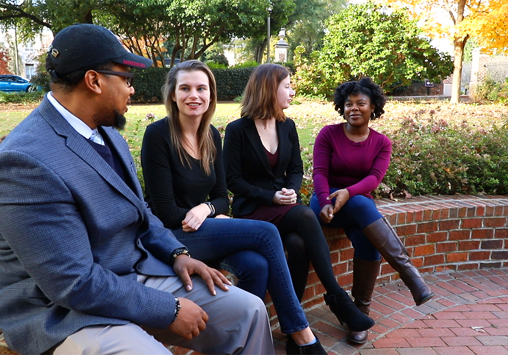 Group of students sitting on a brick wall outside talking. 