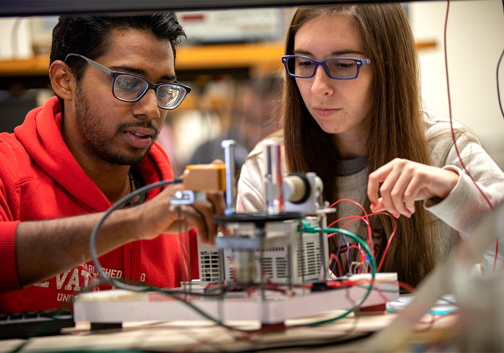 Students wearing safety goggles working on an machine with red and green wires.