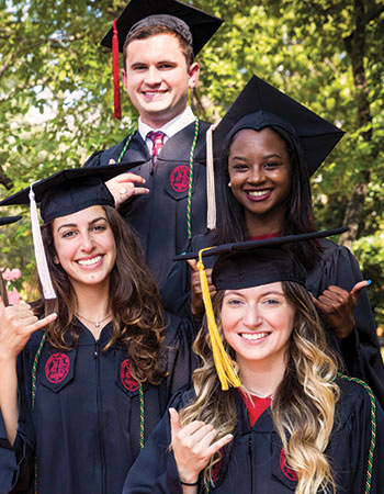 a group of student in caps and gowns are smiling and showing the spurs up gesture