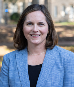 Smiling person in a light blue blazer outdoors on campus.