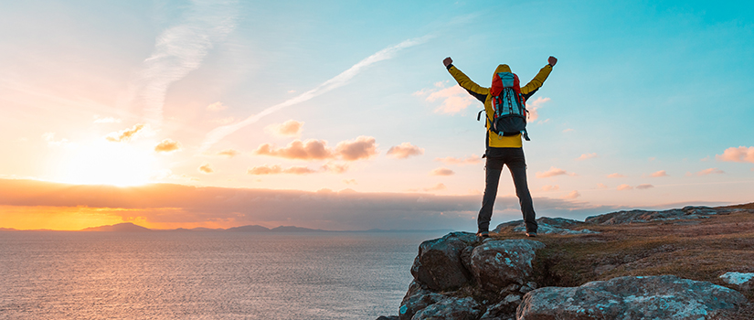 Happy successful man with arms up on the top of cliff in Scotland at sunset