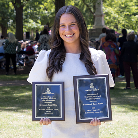 Savannah Miller stands outdoors holding the HRSM Academic Excellence Award and Dean’s Award for Outstanding Leadership at the University of South Carolina.