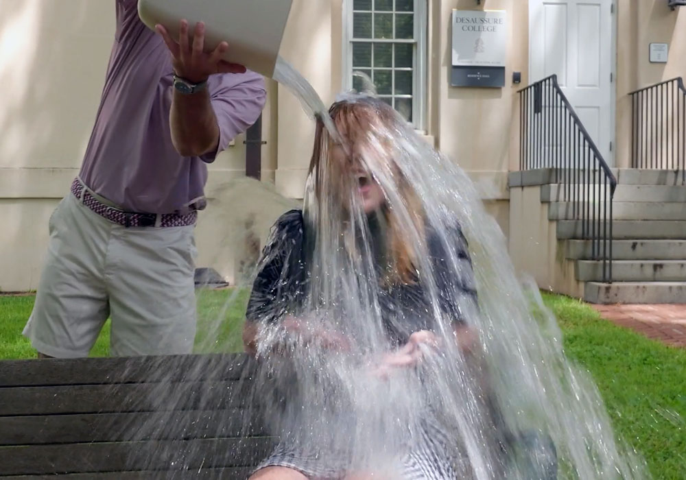 two people outside with one pouring water over the other's head