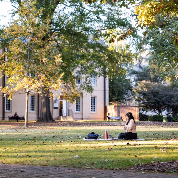 Student sitting on the lawn on the Horseshoe on her phone.
