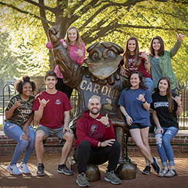 A group of students surround the larger-than-life bronze Cocky statue, all of them flashing the spurs up hand sign.