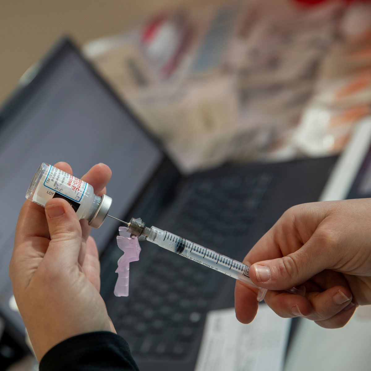 A closeup of a medical professional extracting a vaccine from a vial using a syringe