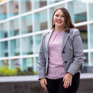 School of Music senior Madie Willard stands in front of the Koger Center wearing a gray jacket and pink top