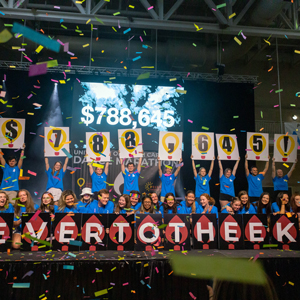 students hold up signs to reveal fundraising for dance marathon signs spell out $788,645! and Forever to thee kids