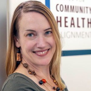 woman stands next to a wall with a sign that reads community health