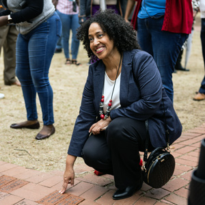 a woman leans down and points to bricks on a walkway