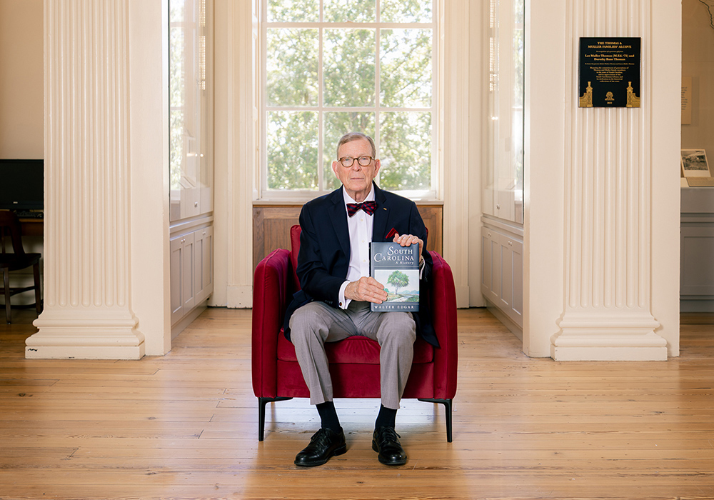 Walter Edgar sits in a red chair and holds his book "South Carolina: A History."